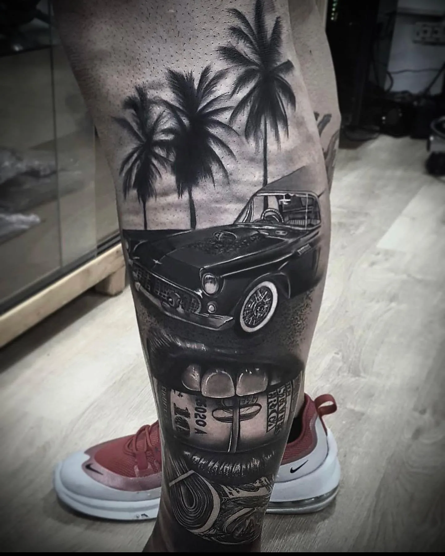 Realistisches Tattoo mit Oldtimer und Palmen über einem Mund-Motiv am Unterschenkel.