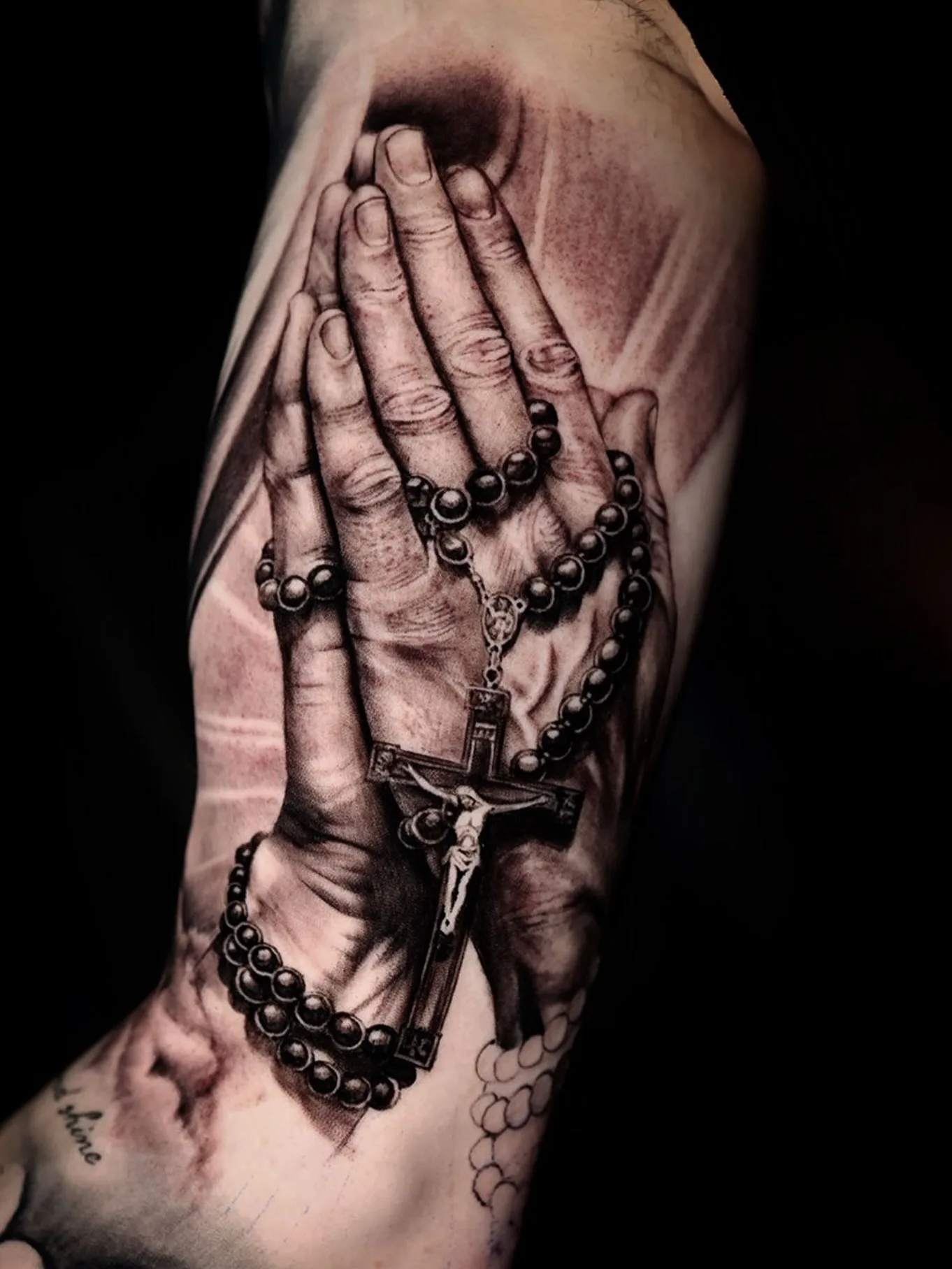 Betende Hände mit Rosenkranz und Kruzifix, Black-and-Grey-Tattoo am Oberarm.